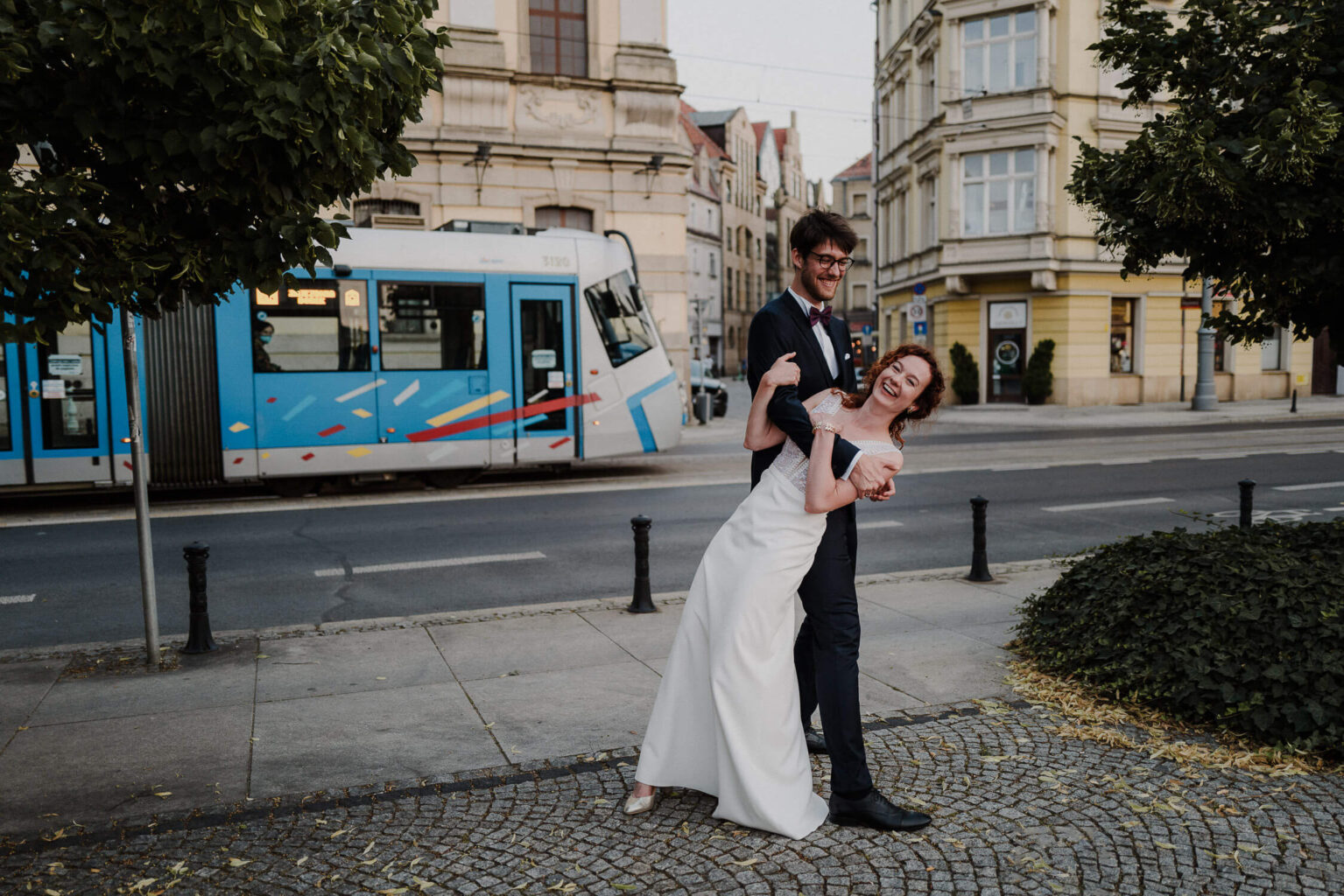 Para młoda pozuje na tle przejeżdżającego tramwaju podczas sesji ślubnej we Wrocławiu
